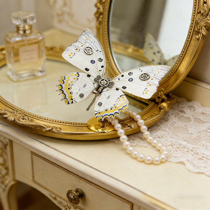 An elegant steampunk puzzle, a mechanical butterfly with delicate white and yellow wings adorned with gears, gracefully stands on a vintage dressing table alongside a pearl necklace, a perfume bottle, and an ornate mirror. This exquisite metal model is a charming example of mechanical steampunk artistry, serving as a lux