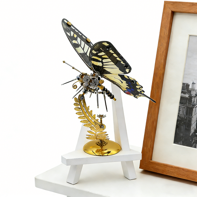 A stunning steampunk puzzle, a majestic mechanical swallowtail butterfly with intricate black, yellow, and white wings, beautifully displayed on a golden stand next to a small white easel and framed art. This impressive metal model showcases exceptional mechanical steampunk design, making it an ideal 3D puzzle Metal Kit for hobbyists or a captivating steampunk mech decorative piece that blends art and engineering.