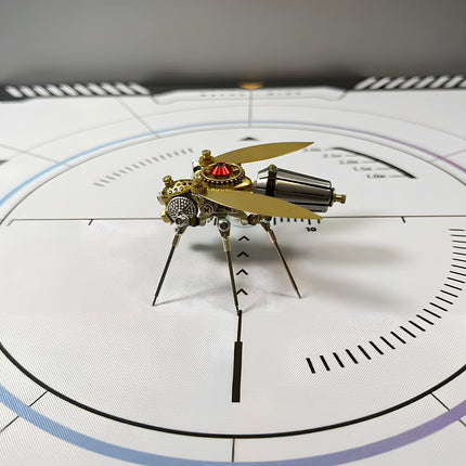 Side view of a meticulously crafted steampunk fly 3D puzzle metal kit on a white measurement grid, showcasing its golden wings, a dark, segmented abdomen, and intricate mechanical steampunk details with a prominent red gem.