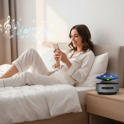 A woman reclines on her bed using a smartphone, while a magnetic levitation flying saucer speaker with blue-green light hovers on the nightstand — modern wireless bedside decor