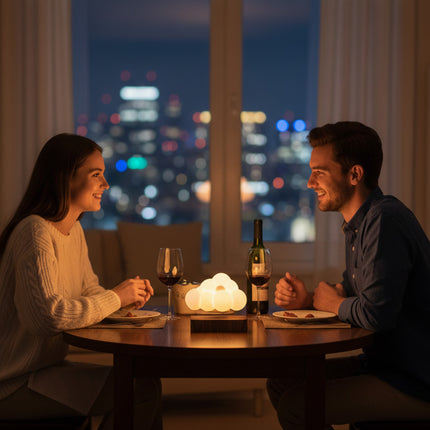 A couple enjoys a romantic dinner under the city lights, with a cloud-shaped warm-glow ambiance lamp placed at the center of the table, resting on a magnetic levitation wooden base.