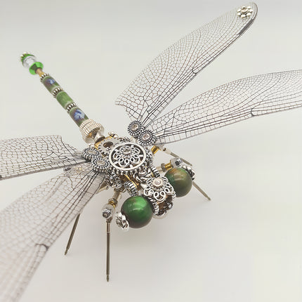 This is a detailed close-up of the finished Tablefunny steampunk dragonfly 3D metal puzzle: Made of silver-toned metal, its wings replicate the dragonfly’s delicate textures, with green bead decorations embedded in the head. The body is densely adorned with steampunk elements like gears and carved metal components, while the tail features green and blue accents. Rich in mechanical details and exquisite craftsmanship, it’s a craft that blends assembly fun and decorative value.