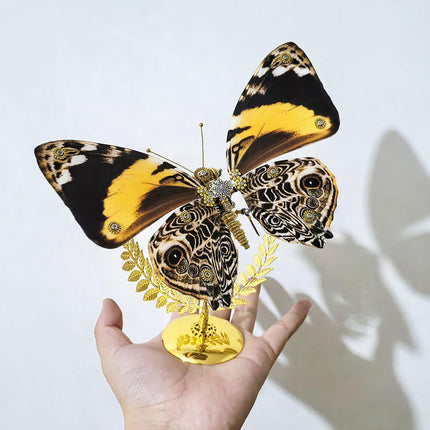 A stunning steampunk puzzle, a magnificent mechanical butterfly with vibrant black, yellow, and intricate patterned wings, delicately held in a person's hand on its golden stand. This exquisite metal model highlights sophisticated mechanical steampunk design, making it an impressive 3D puzzle Metal Kit for hobbyists or a captivating, handheld steampunk mech decorative piece that showcases its unique coloration and detailed craftsmanship.