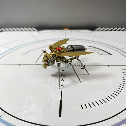 Angled front view of a mechanical steampunk fly 3D puzzle metal kit on a white measurement mat, showcasing its golden wings, a dark segmented abdomen, and intricate mechanical details with a bright red central gem. This steampunk puzzle is a remarkable display piece.