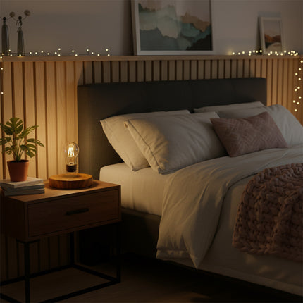 A cozy bedroom scene: A warm yellow glow emanates from a magnetic levitation bulb resting on a wood-grain magnetic levitation base atop the nightstand, flanked by succulent plants and decorative string lights — a modern anti-gravity bedside ambiance lamp