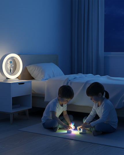 Two children played on the bedroom floor at night, while a warm white magnetic levitation astronaut nightlight floated above the nightstand. Inside the ring-shaped lamp, an astronaut figurine hovered
