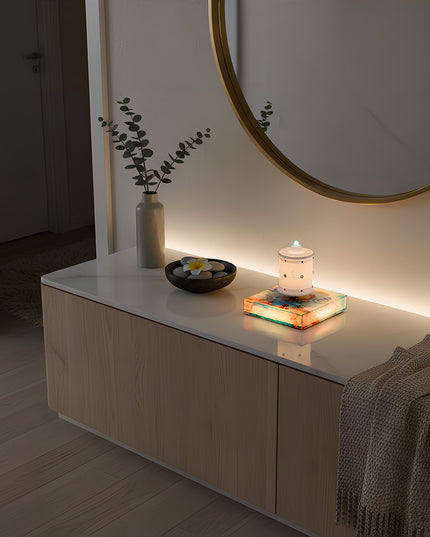 The levitating Zen lamp rests atop a magnetic base beneath a circular mirror, positioned on a marble countertop storage unit. Adjacent are a vase, decorative stones, and a knitted throw blanket — creating a modern home ambiance
