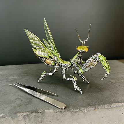  A finely detailed green and silver steampunk mech praying mantis maquette en metal with translucent wings, poised on a concrete surface next to a pair of tweezers. This intricate 3D metal model kit is a challenging steampunk puzzle, emphasizing precision assembly.