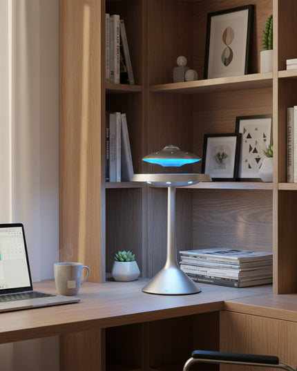 The magnetic levitation Bluetooth UFO floats atop a silver pillar base, positioned beside a corner desk in a modern home study; emitting a blue ambient glow, it's perfect for focused work and setting the mood