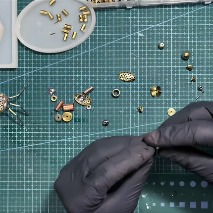 Hands in black gloves meticulously assembling small metal parts for a 3D puzzle metal model, a DIY metal kit, on a green cutting mat. This intricate process promises a rewarding build, resulting in a unique and funny table display.