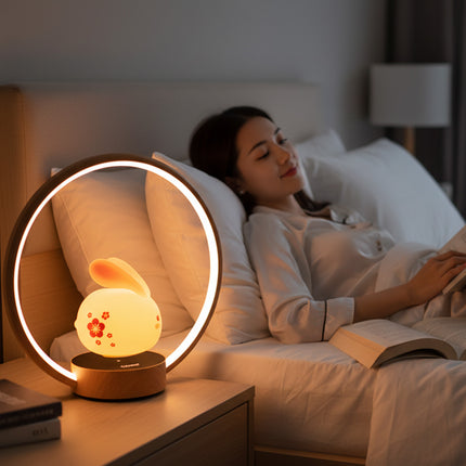 Levitating bunny LED night light inside a wooden ring lamp on a bedside table, casting soft warm, non‑glaring light