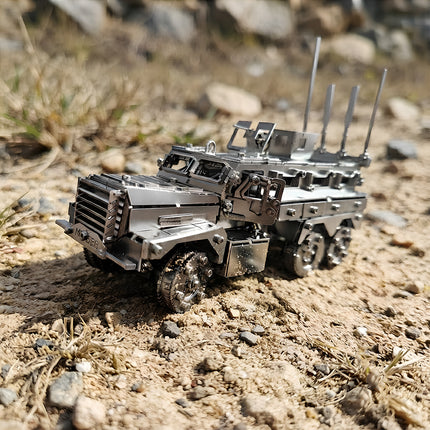 A detailed 3D metal armored military truck model sitting on rough sand and rocky outdoor terrain under natural light.