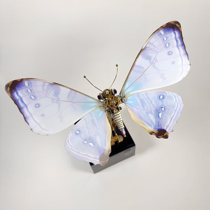 Top-down view of an assembled 3D metal mechanical butterfly model puzzle with purple and blue painted wings on a white background.