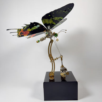 Side profile view of an assembled 3D metal mechanical butterfly model puzzle on a black display base.