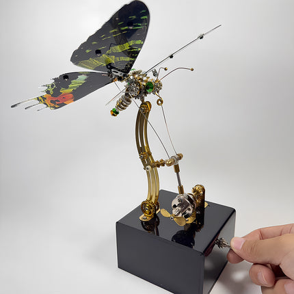 Hand operating the metal toggle switch on the base of an assembled 3D metal mechanical butterfly model puzzle.
