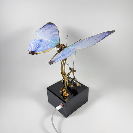 Assembled blue 3D metal mechanical butterfly model puzzle featuring a USB-powered black base and moving gears.