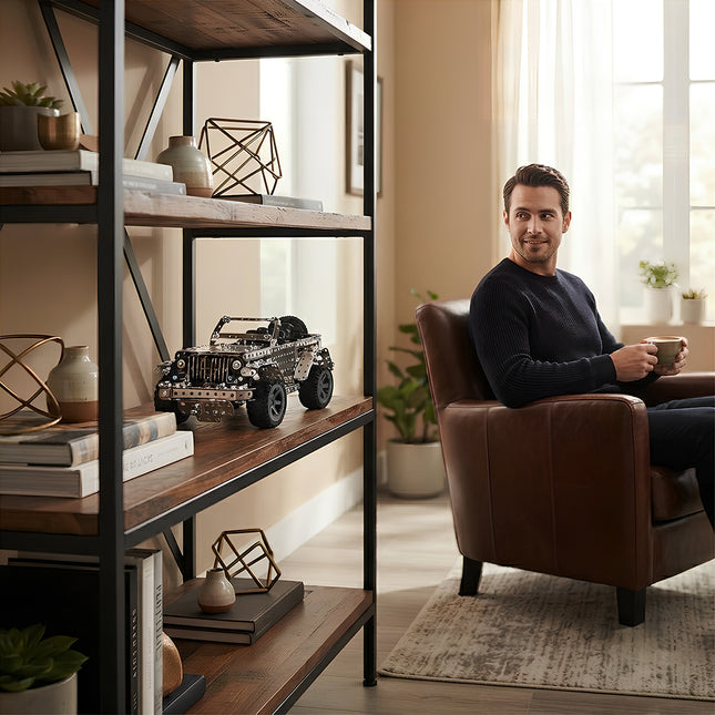 A man relaxing in a leather armchair in a cozy living room while looking at a finished 3D metal off-road vehicle model displayed on an industrial bookshelf.