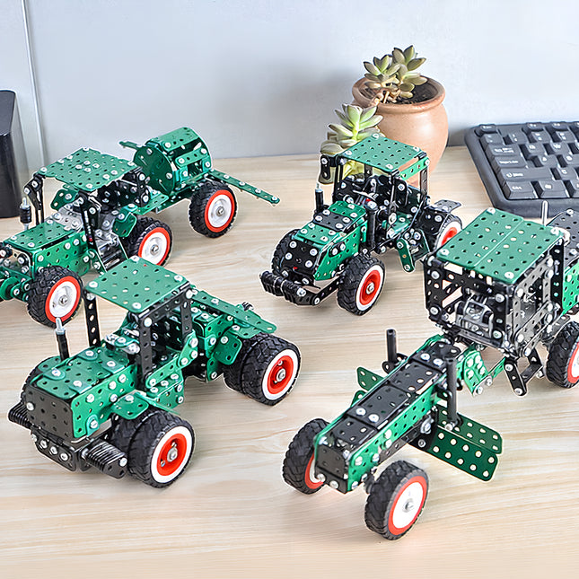 A group lifestyle photograph of four completed green stainless steel vehicle models including tractors and a grader on a wooden desk.