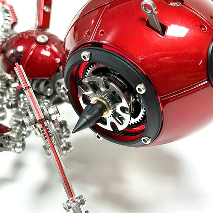 Close-up of the red mechanical spider metal model's spherical body, highlighting its glowing gears, pointed tip, and connected mechanical steampunk legs. This 3D puzzle metal kit features intricate components for a detailed steampunk puzzle.