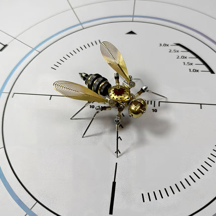 Overhead view of a mechanical steampunk bee 3D puzzle metal kit, showcasing its intricate golden filigree wings, segmented body, and detailed gears on a white measurement surface. This steampunk puzzle is a work of art.