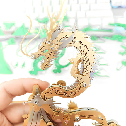 Hand holding a majestic gold and silver steampunk dragon metal model 3D puzzle, showcasing its intricate design against a blurred background of green components, an engaging mechanical steampunk puzzle and premium Metal Kits.