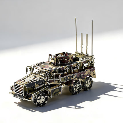 A high-angle left front 3/4 view of a completed camo 6x6 tactical armored vehicle metal puzzle, displaying the detailed roof armor, rotatable weapon turret, rear antennas, and steel wheels with realistic shadows.