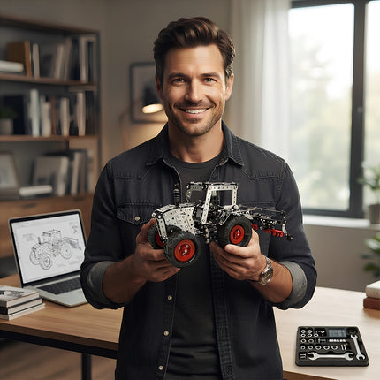 Front view of a satisfied enthusiast presenting a fully assembled metallic tractor model kit with red wheels next to a laptop displaying blueprints.