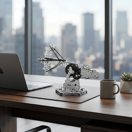 Fully assembled metallic mechanical ballista model displayed on a modern wooden office desk next to a laptop and coffee mug.