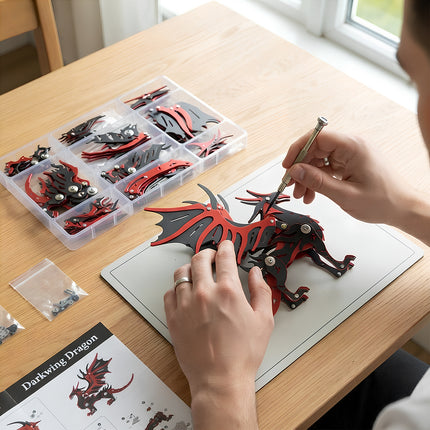 Person assembling a red and black metallic dragon puzzle with manual, tools, and compartmentalized parts storage box.