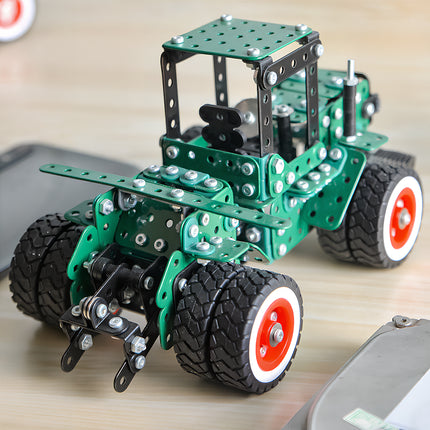 A close-up lifestyle photograph focusing on the rear hitch mechanism and double wheels of a green metal tractor model kit on a light wood tabletop.