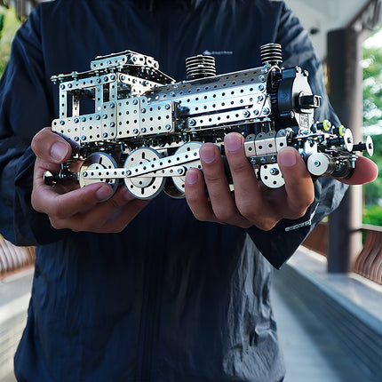 Hands holding a completed steampunk puzzle metal model of a vintage mechanical train for size reference