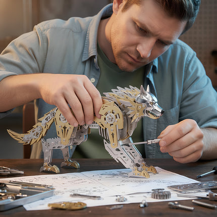 A man using a screwdriver to assemble a gold and silver 3D metal mechanical wolf model over assembly blueprints.
