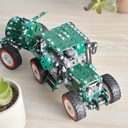 A completed green metal water truck model kit with a spray trailer displayed as desktop decor on a wooden table next to a succulent plant.