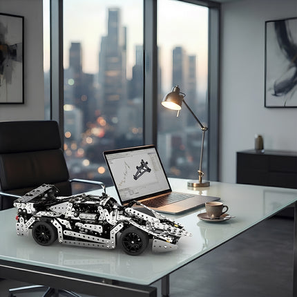 Intricate metallic sports car puzzle model placed next to a laptop displaying 3D engineering designs on a sleek office desk.