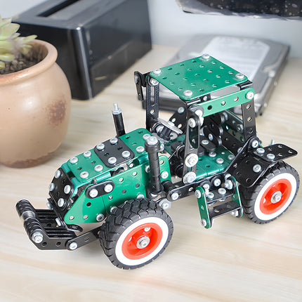 A completed modern green metal tractor model kit displayed as a desk toy on a wooden table next to a succulent plant.