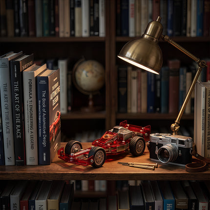 A classic metal model racing car displayed on a wooden bookshelf desk next to a vintage desk lamp and camera.